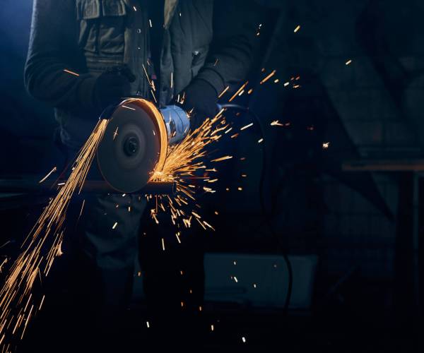 Close up of fitter in special suit cutting with rotating disc for metal with large sparks. Concept of process polishing or welding metal with flash sparks in factory.